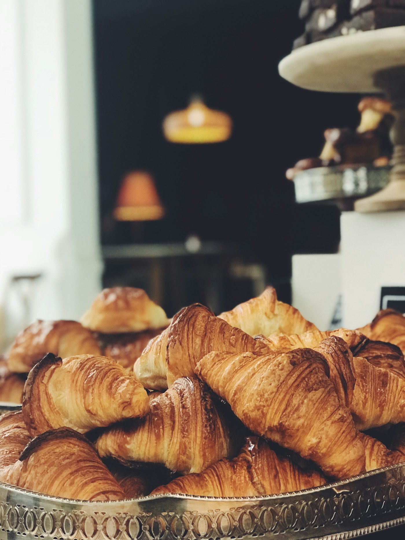 A pile of golden croissants on a silver stand in the bakery window