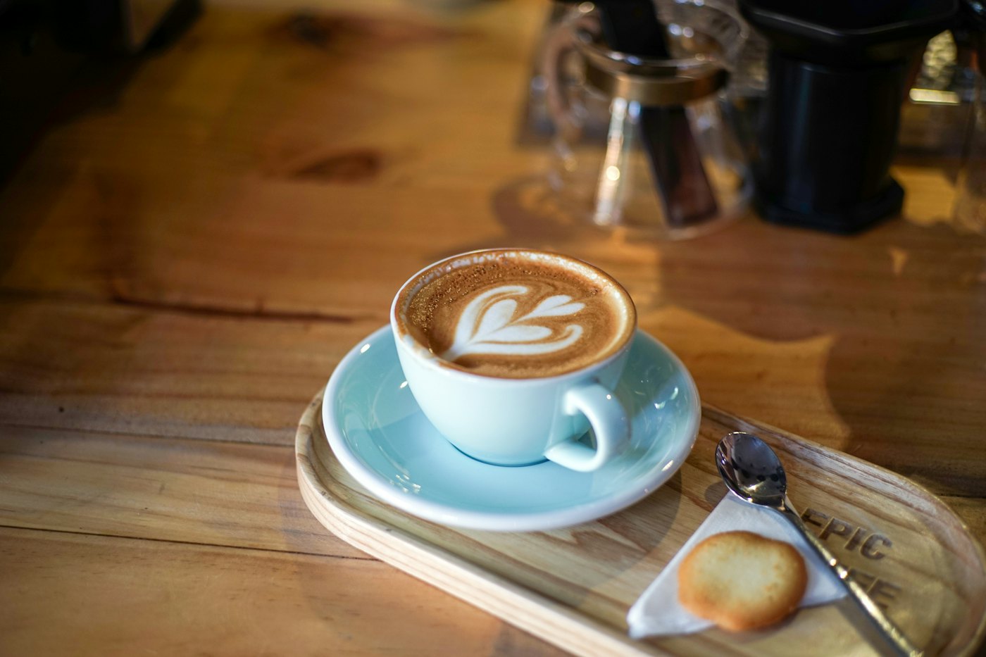 A latte with a leaf poured into the foam, in a pale blue cup on a wooden counter