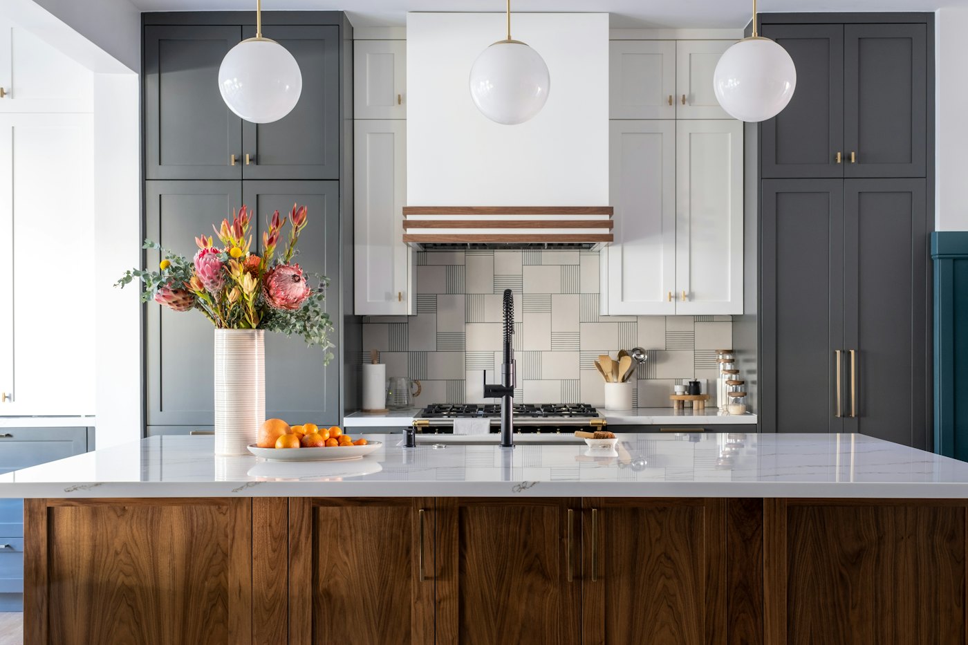 Finished kitchen with a walnut island, dark green-grey cabinets, three globe pendant lights and a patterned tile backsplash behind the range.