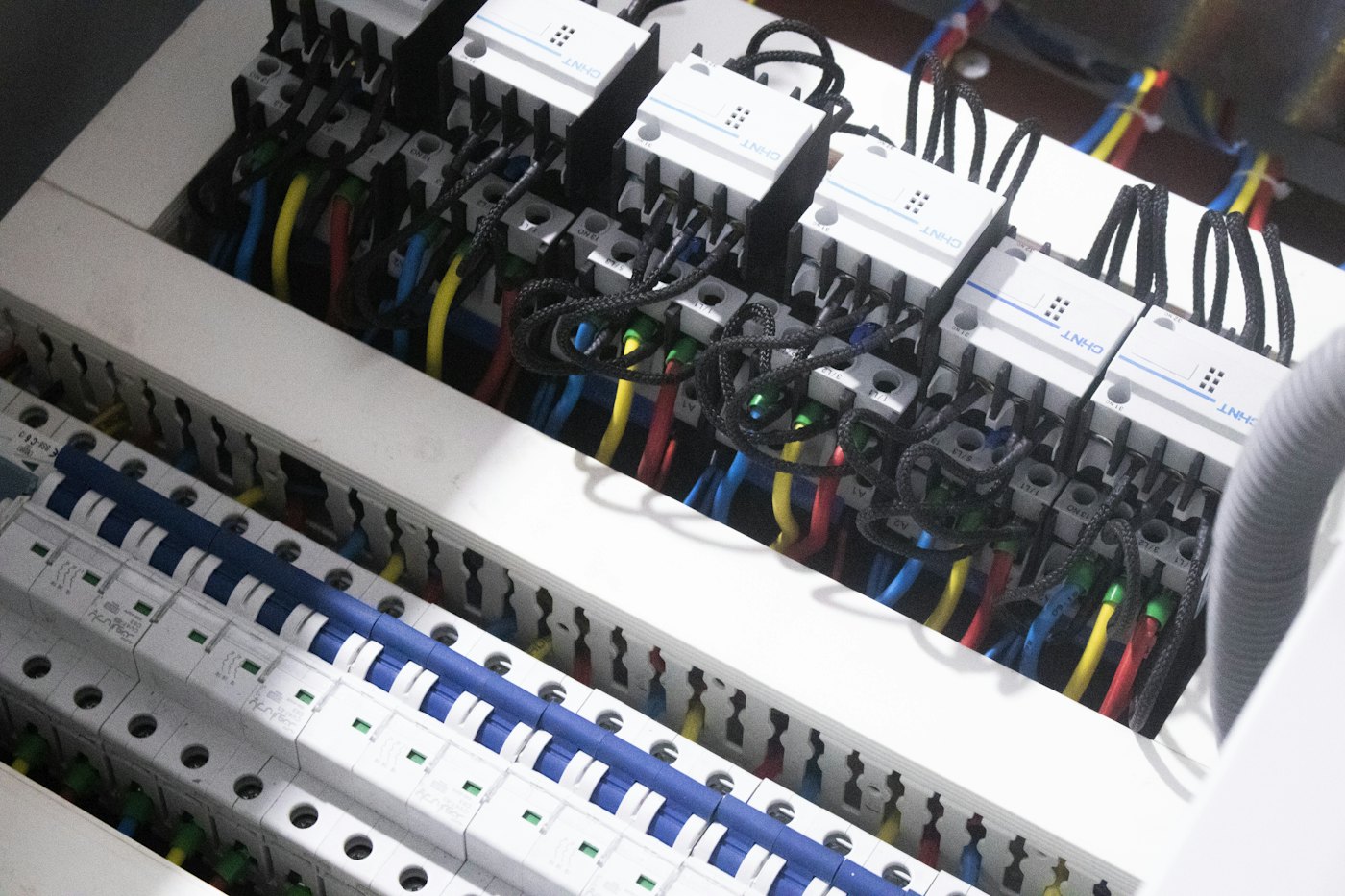 Close view inside an electrical panel: rows of white breakers and blue, yellow and red wires routed neatly through a slotted duct.
