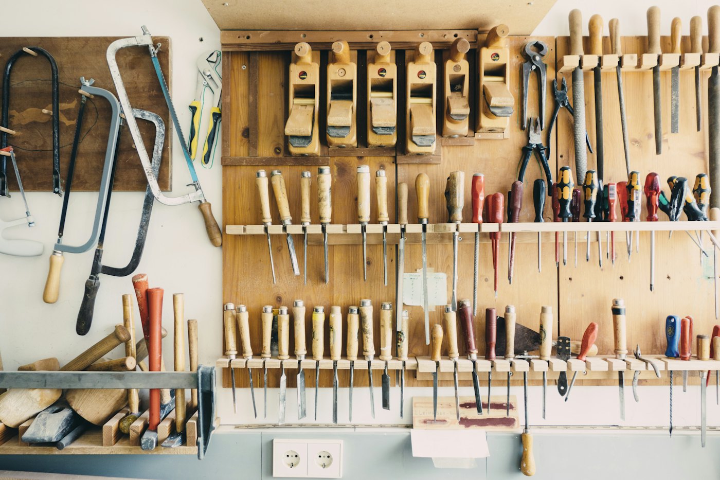 A workshop wall with hand saws, wooden planes, chisels and screwdrivers hung in neat rows on racks.