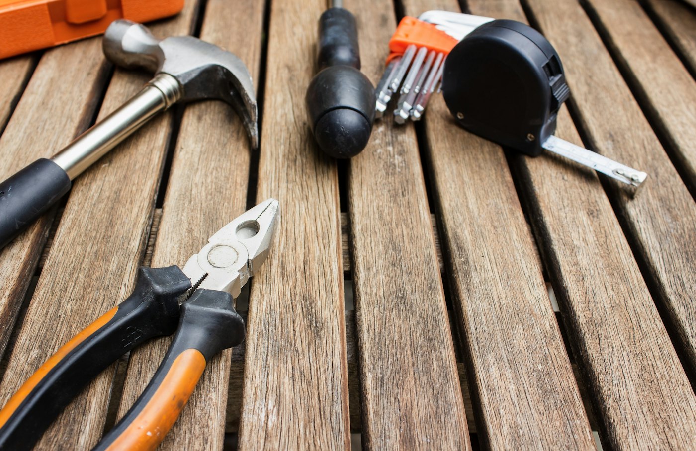A claw hammer, pliers, a screwdriver, hex keys and a tape measure laid out on weathered wood decking.