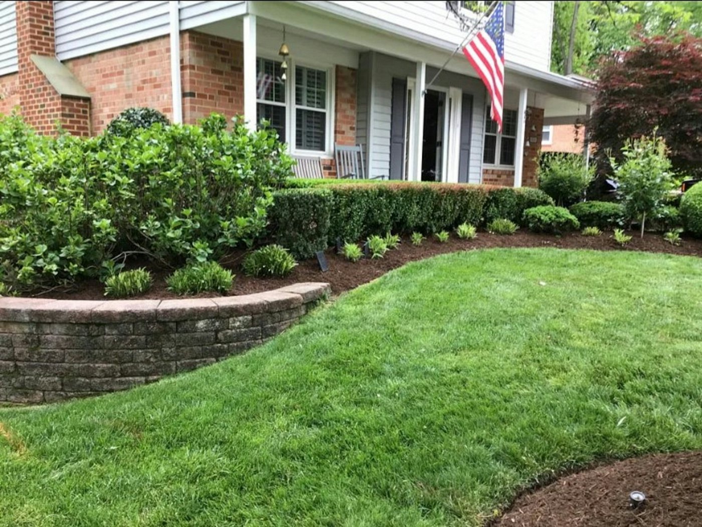 Brick house with a freshly mowed front lawn, a clean edge along the mulch bed and trimmed shrubs above a low stone wall