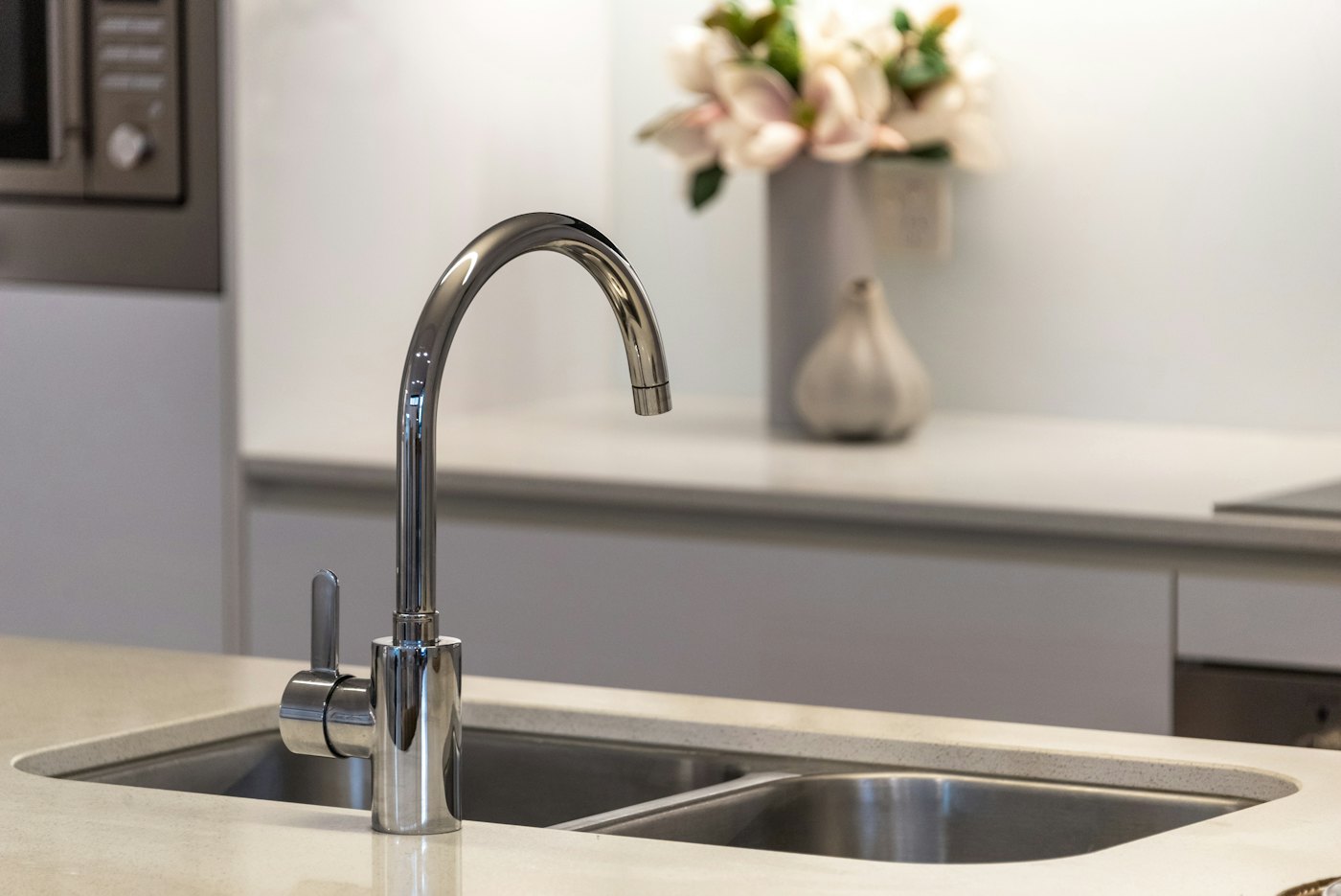 A stainless gooseneck kitchen faucet over a double sink set in a pale counter