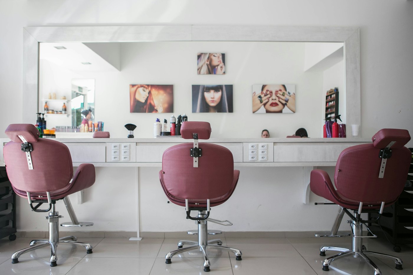 Maroon salon chairs lined up at a long white counter under a wide mirror.